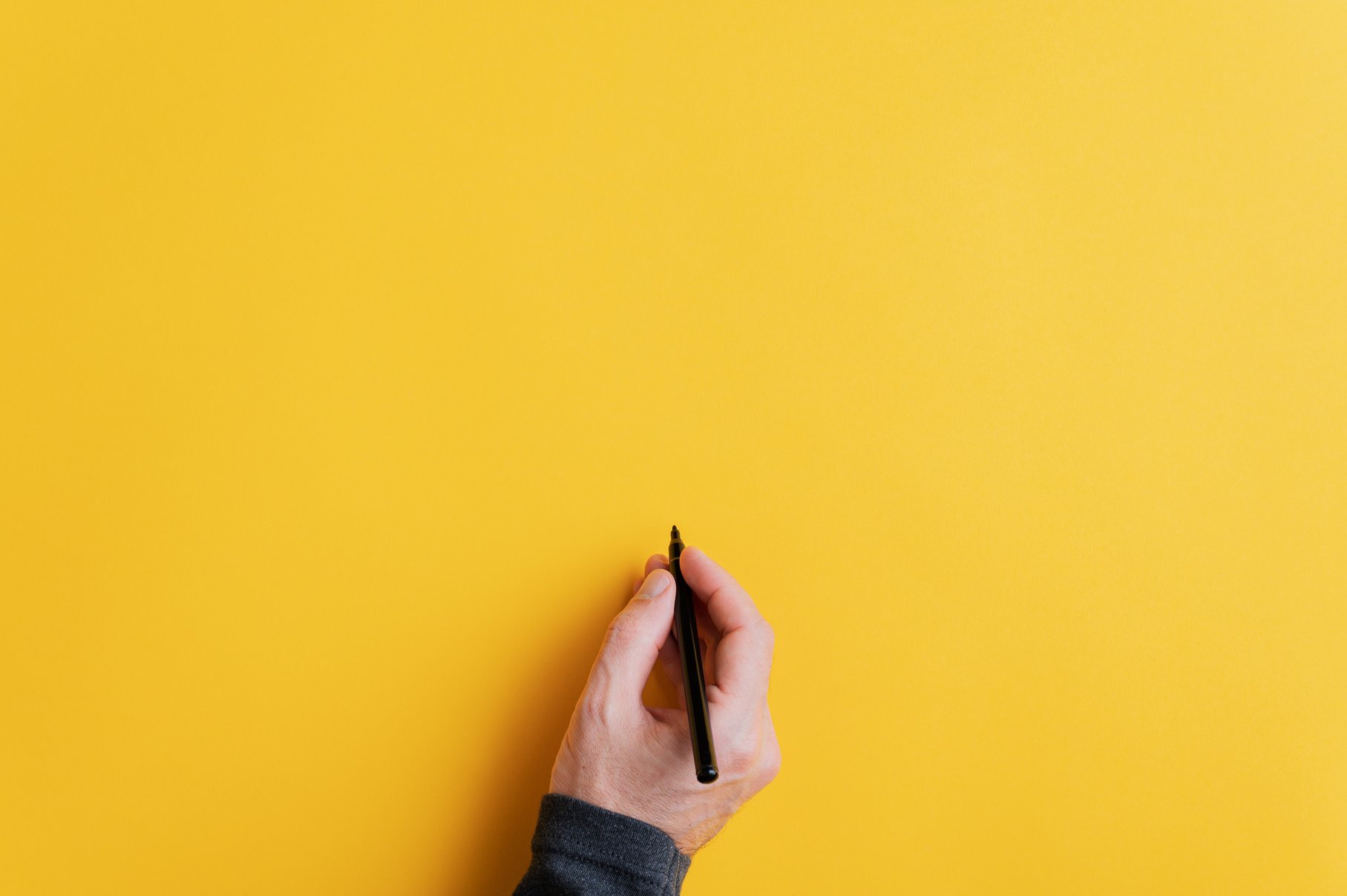 Male Hand Writing on a Blank Yellow Surface with Black Marker